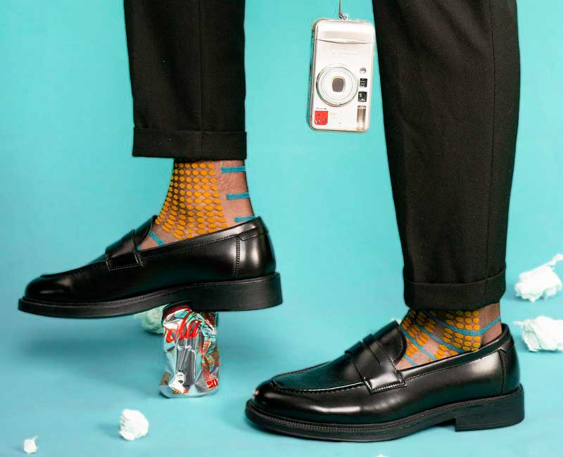 calcetas-geometricas-moda-hombre-capitan-style Calcetas con patrón geométrico y zapatos clásicos negros sobre fondo turquesa – Capitán Style en Bodega Italia