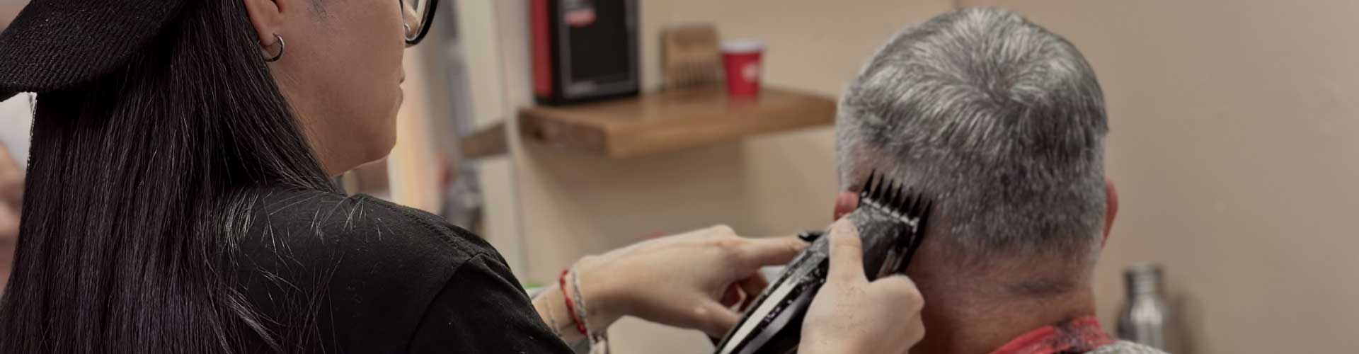 pols-barber-corte-cabello-hombre-mayor-providencia Barbera de Pols Barber realizando un corte de cabello con máquina a un hombre de pelo canoso en Bodega Italia, Providencia.