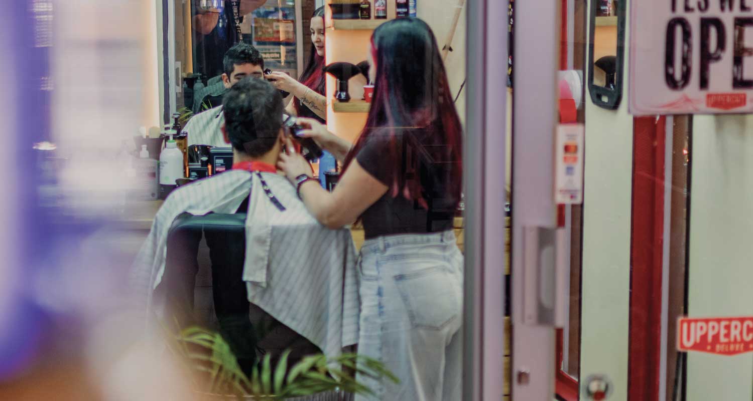 pols-barber-corte-cabello-masculino-providencia Barbera de Pols Barber realizando un corte de cabello masculino con máquina, en el interior de la barbería en Bodega Italia
