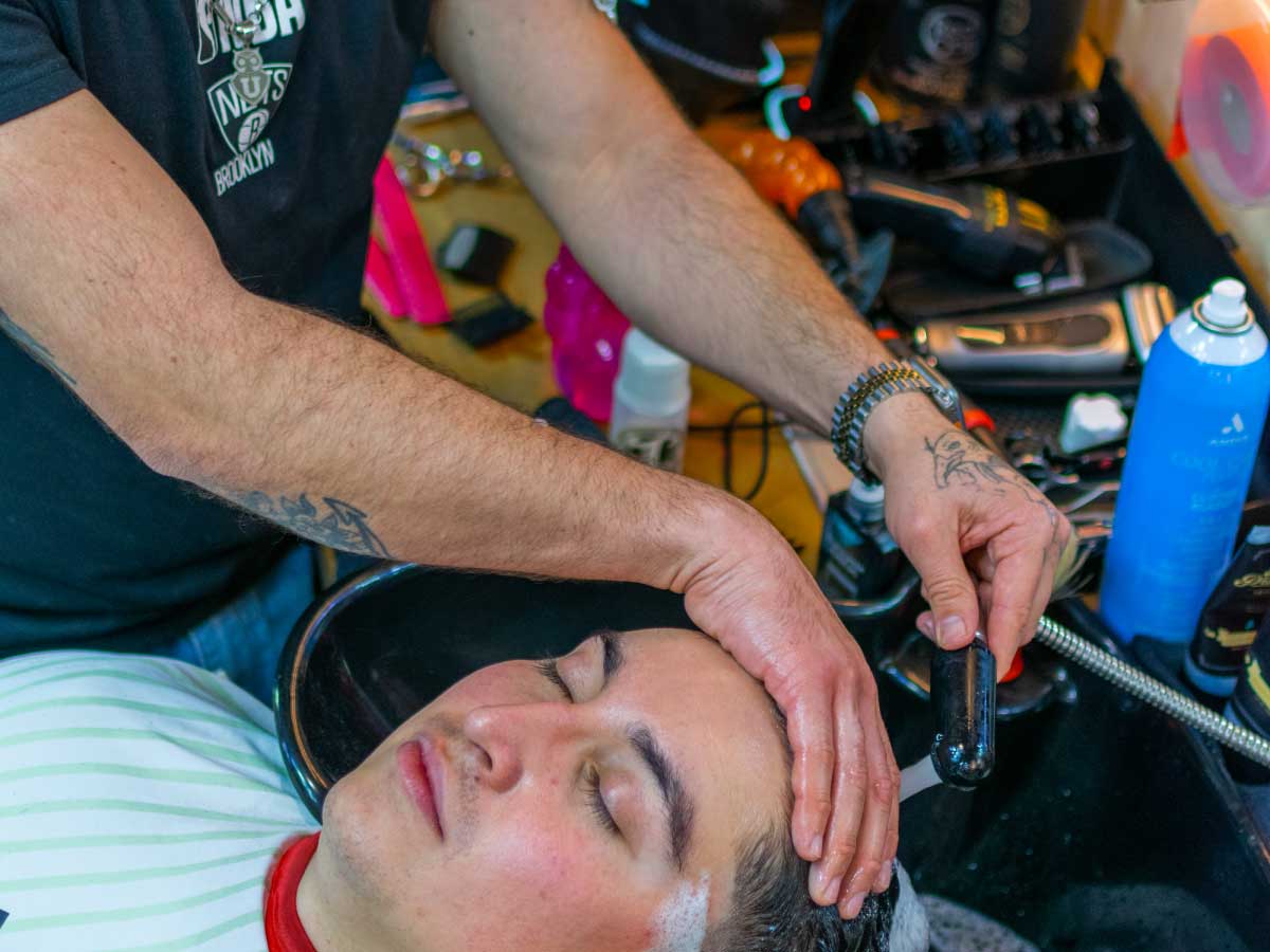 pols-barber-lavado-capilar-masculino-providencia Barbero realizando lavado de cabello y masaje capilar a un cliente en Pols Barber, barbería ubicada en Bodega Italia, Providencia.