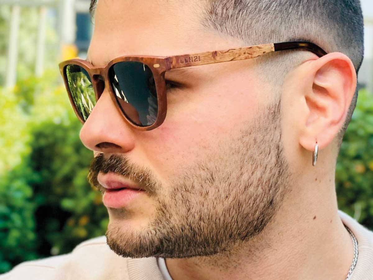 zamu-gafas-sol-madera-estilo-hombre-diseno-chileno Primer plano de hombre usando gafas de sol con marco de madera y aro plateado, estilo urbano con detalles de ZAMU en Barrio Italia