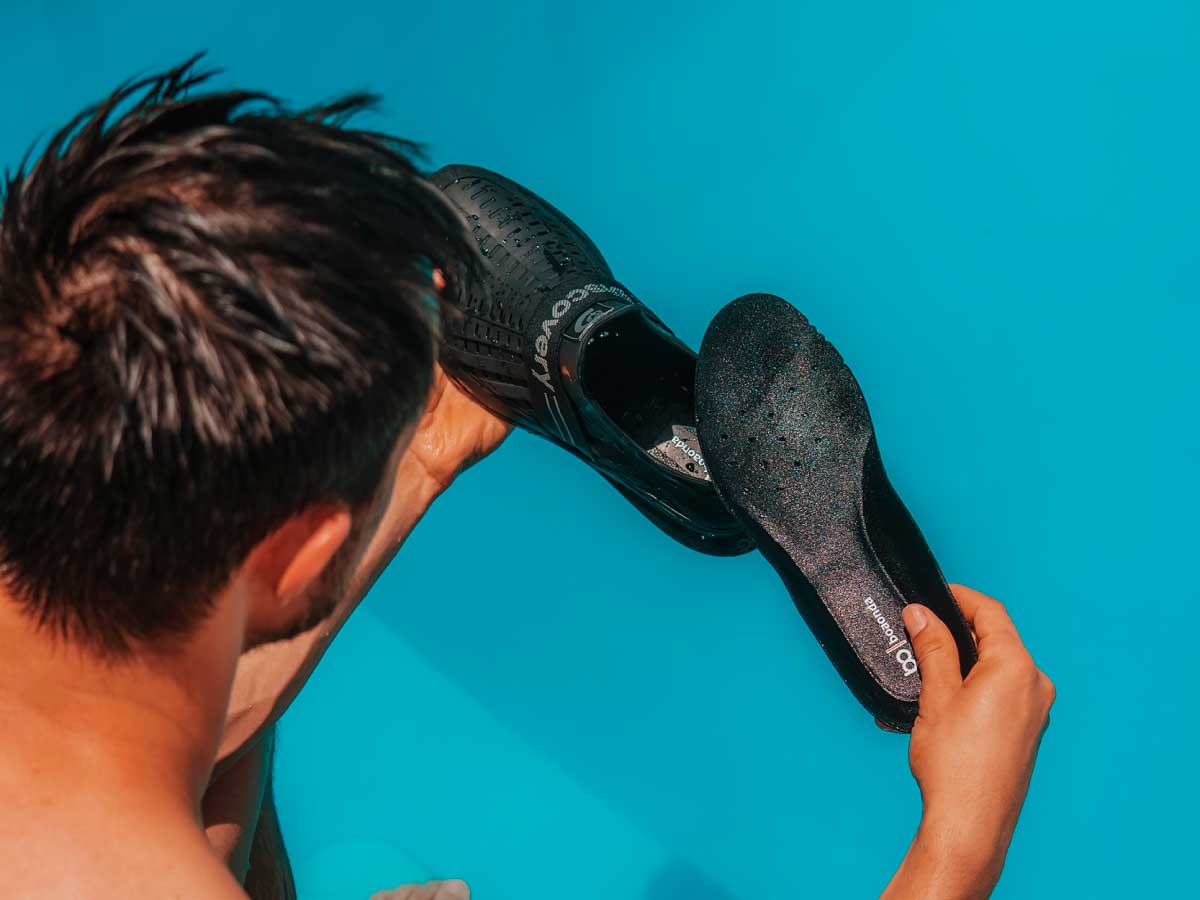 zapatillas-verano-hombre-piscina-del-basto Hombre sosteniendo zapatillas impermeables negras de DEL BASTO junto a una piscina